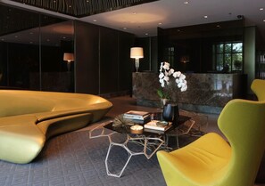 A modern lobby with a reception desk, a seating area with yellow chairs, and a decorative table with books and a vase of flowers. - Tropical Retreat • 24F Balcony • Sauna • Gym • Greenbelt • Makati (Makati)