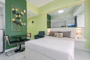 A hotel room with a bed, a desk, and a chair. There is a large mirror on the wall and a window with a view. - Tropical Retreat • 24F Balcony • Sauna • Gym • Greenbelt • Makati (Makati)