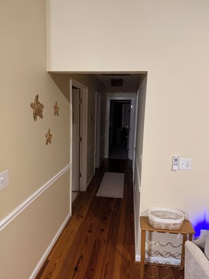 A hallway with wooden flooring, a white door, and a small table with a basket on it. - Serene Mediterranean 4-bedroom beach house minutes from the water in Oak Island (Oak Island)