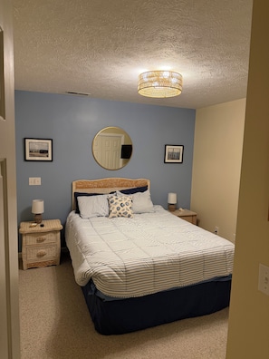 A bedroom with a bed, a bedside table, a lamp, a mirror, and two framed pictures on the wall. - Serene Mediterranean 4-bedroom beach house minutes from the water in Oak Island (Oak Island)