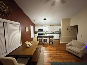 A modern kitchen with white cabinets, a central island with bar stools, and a dining area with a wooden table and chairs. - Serene Mediterranean 4-bedroom beach house minutes from the water in Oak Island (Oak Island)