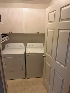 A laundry room with two stacked washers and dryers, a shelf with folded clothes, and a door to another room. - Serene Mediterranean 4-bedroom beach house minutes from the water in Oak Island (Oak Island)