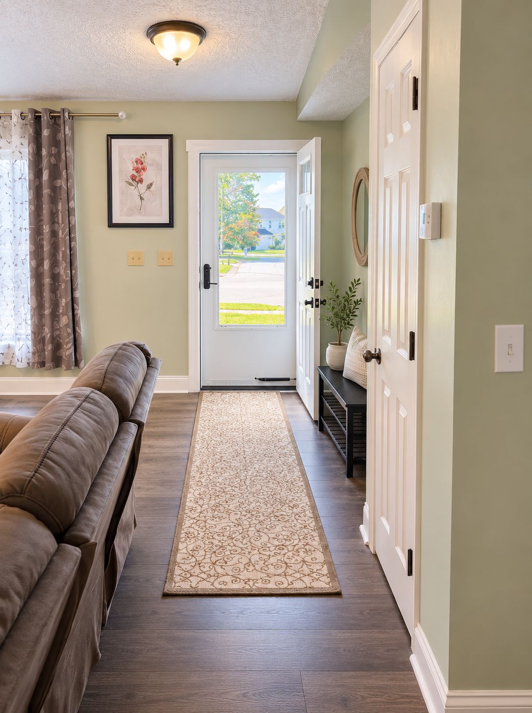 A hallway with a brown leather sofa, a patterned rug, and a door leading outside.