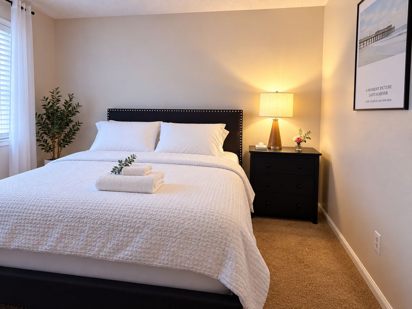 A neatly made bed with white linens, a bedside lamp, and a framed picture on the wall.