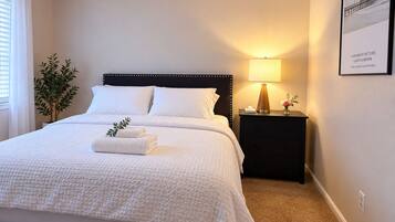 A neatly made bed with white linens, a bedside lamp, and a framed picture on the wall.