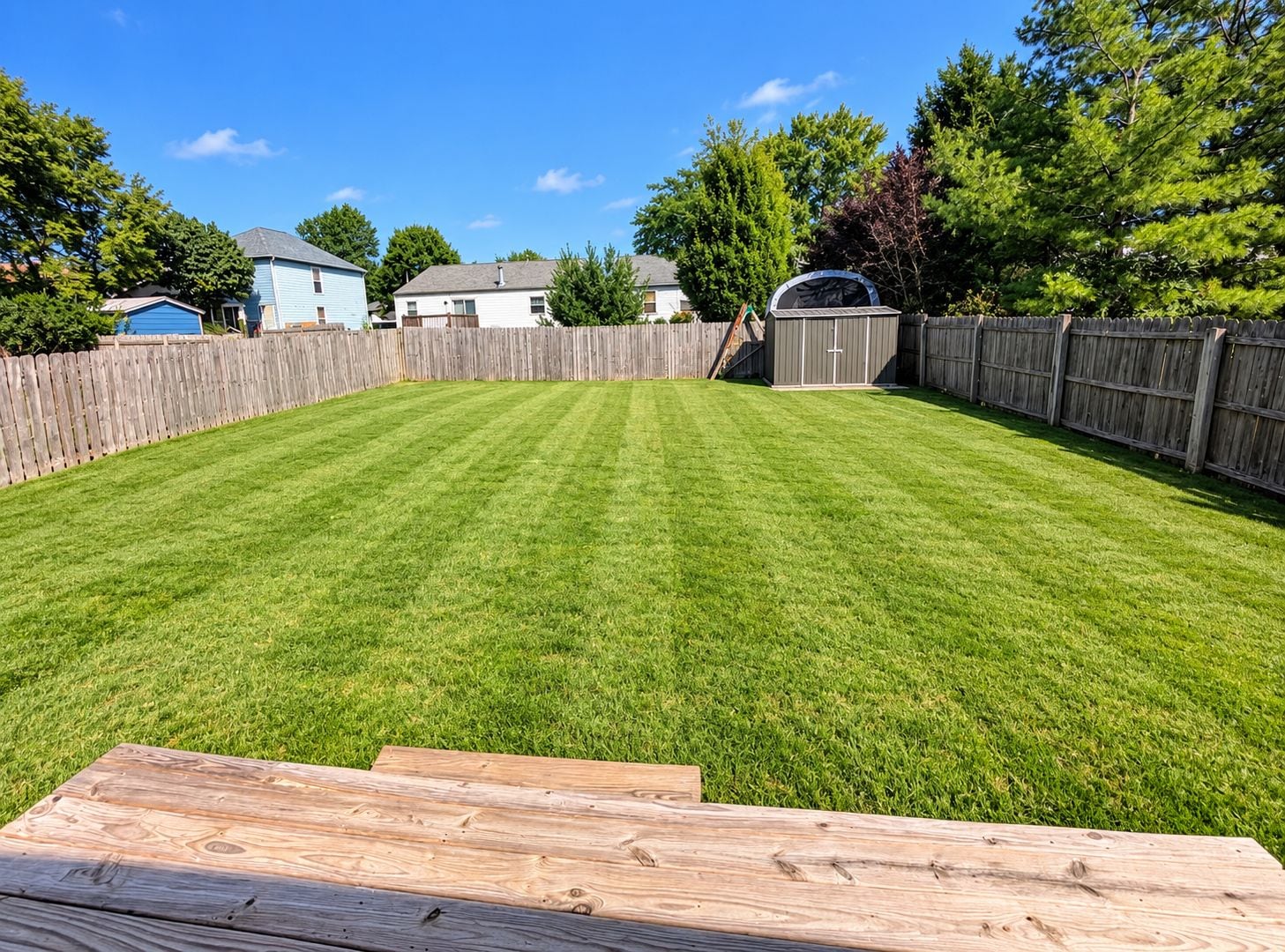 A well-maintained backyard with a wooden deck, a shed, and a wooden fence.