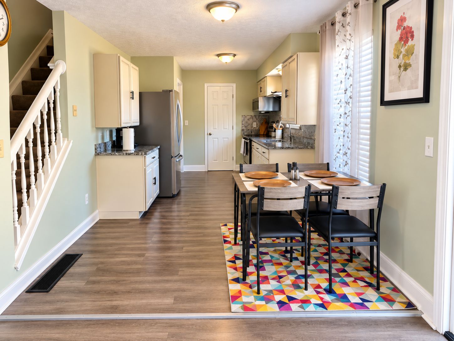 A kitchen with a dining area, wooden flooring, and a colorful geometric rug.