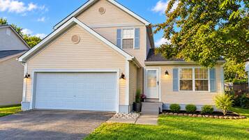 A two-story house with a garage, a front porch with a potted plant, and a well-maintained lawn.