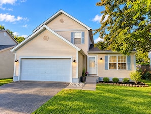 A two-story house with a garage, a front porch with a potted plant, and a well-maintained lawn. - Furnished 3BR Home Near Columbus / Families, Business & Extended Stays (Pickerington)