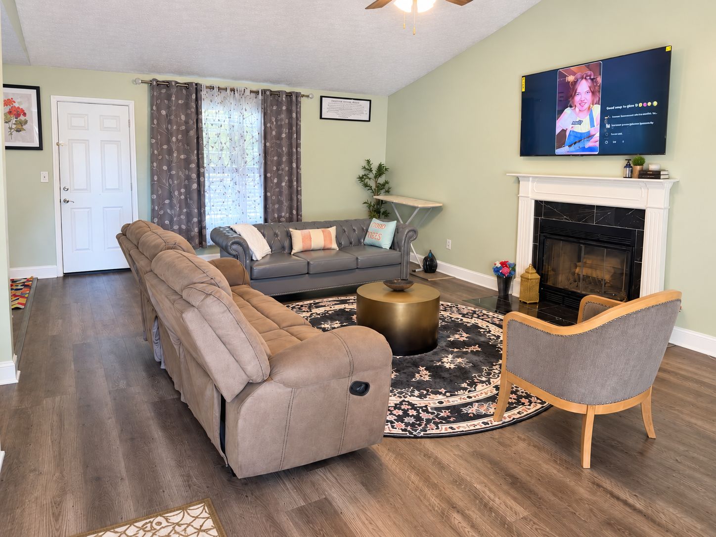 A living room with a sectional sofa, a loveseat, a round coffee table, a fireplace, and a television mounted on the wall.