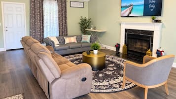 A living room with a sectional sofa, a round coffee table, a fireplace, and a television mounted on the wall.
