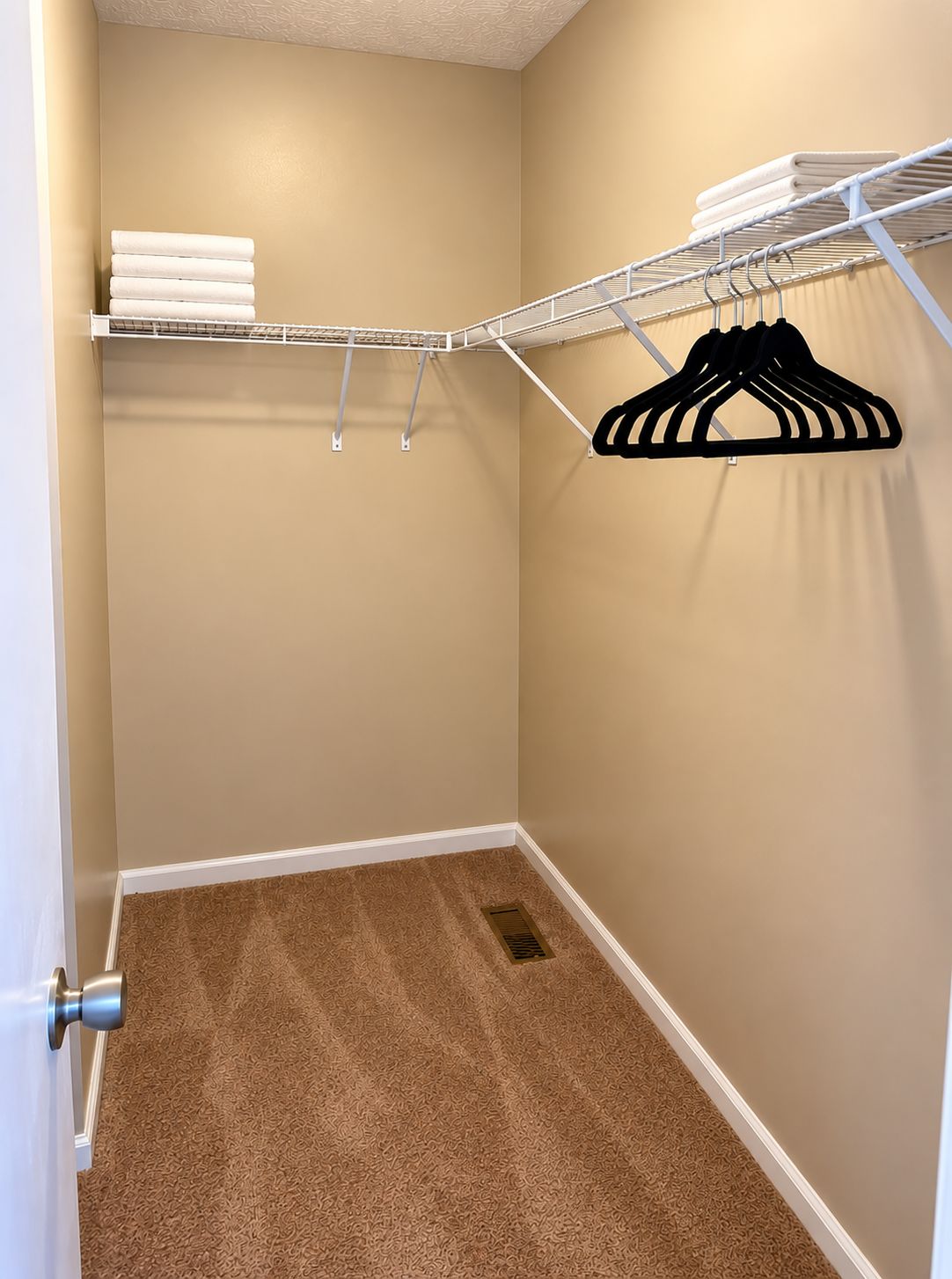 A walk-in closet with a beige carpet, a metal shelving unit with folded towels, and a black hanger.