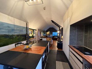 A modern kitchen with a large island, a dining area with a table and chairs, and a living space with a sofa and a TV.