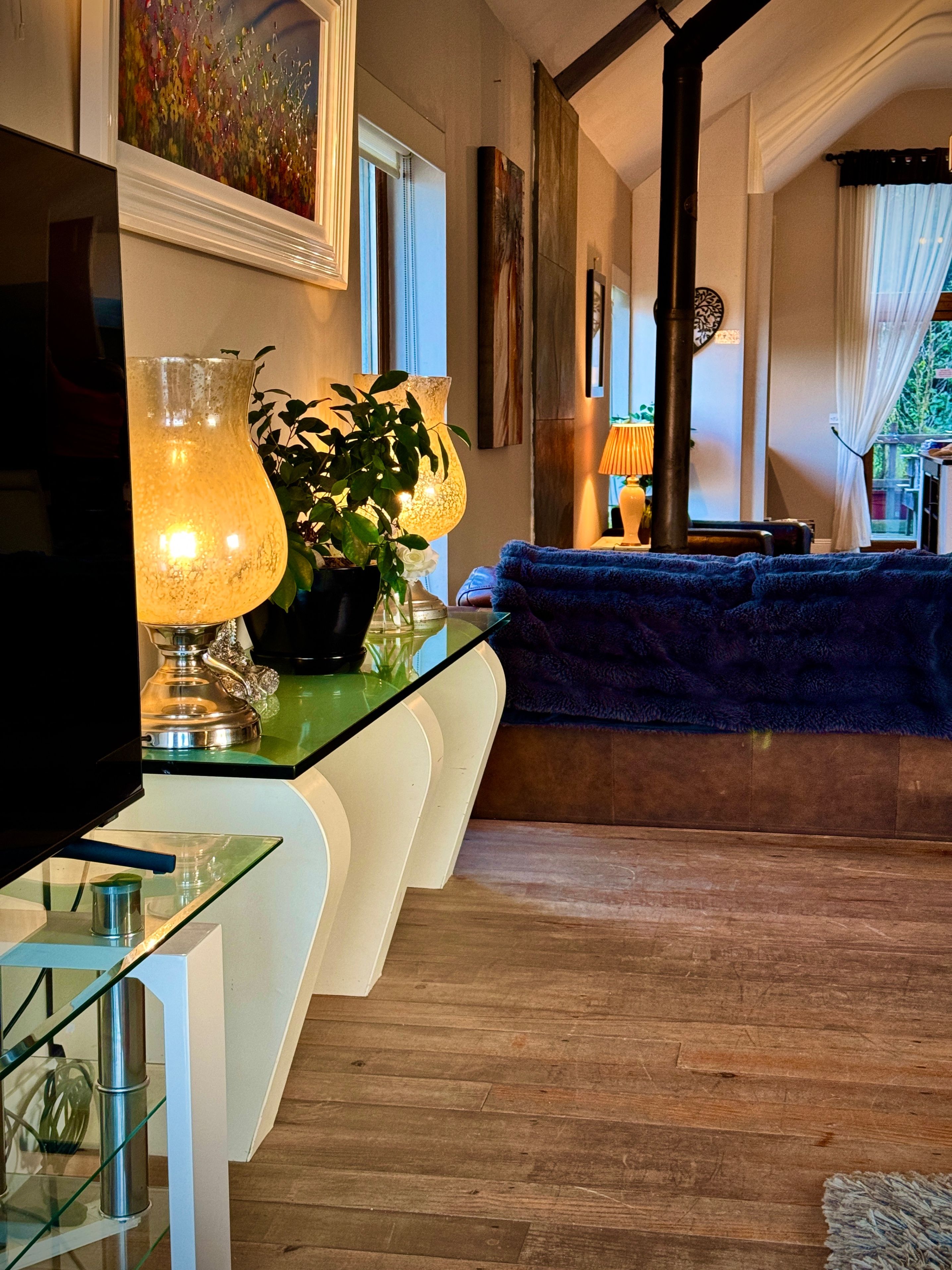 A modern living room with a flat-screen TV, a glass coffee table, a blue sofa, and a decorative lamp.