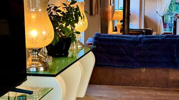 A modern living room with a flat-screen TV, a glass coffee table, a blue sofa, and a decorative lamp.