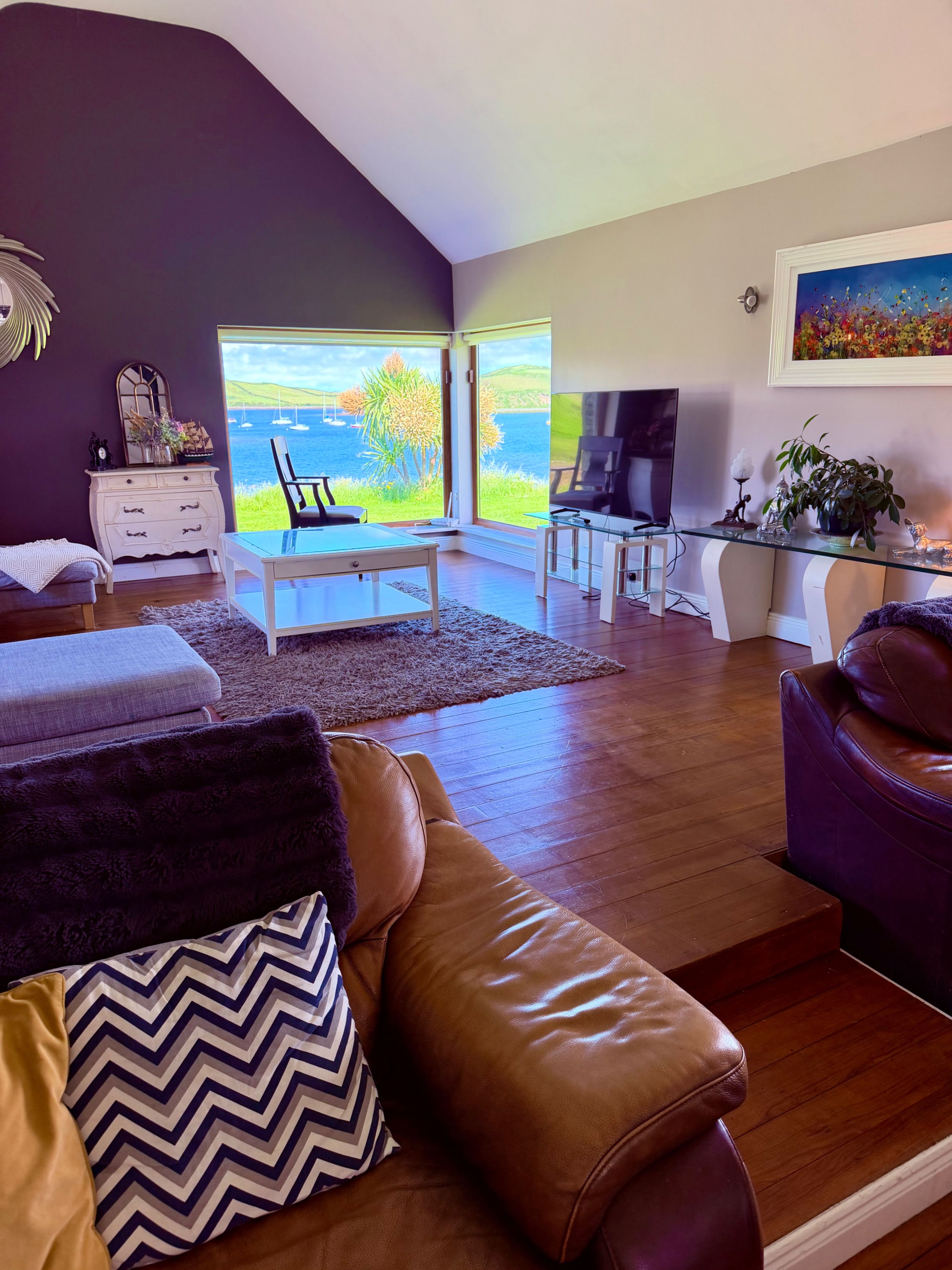A modern living room with a view of the sea, a glass coffee table, leather sofa, and a television.