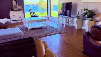 A modern living room with a view of the sea, a glass coffee table, leather sofa, and a television.