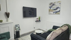A living room with a flat-screen TV mounted on the wall, a sofa, a coffee table, and a fireplace. - Sensational- Haven place (Leicester)