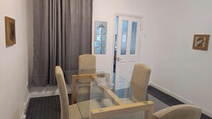 A dining area with a glass table and four chairs, a grey curtain, and a door with a blue frame. - Sensational- Haven place (Leicester)