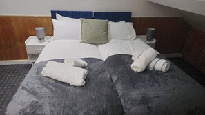 Cama bem arrumada com almofadas, abajur e toalhas dobradas sobre um edredom cinza escuro.