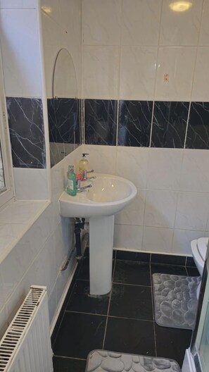 Um banheiro com pia branca, paredes revestidas de azulejos preto e branco, vaso sanitário branco e chão preto.