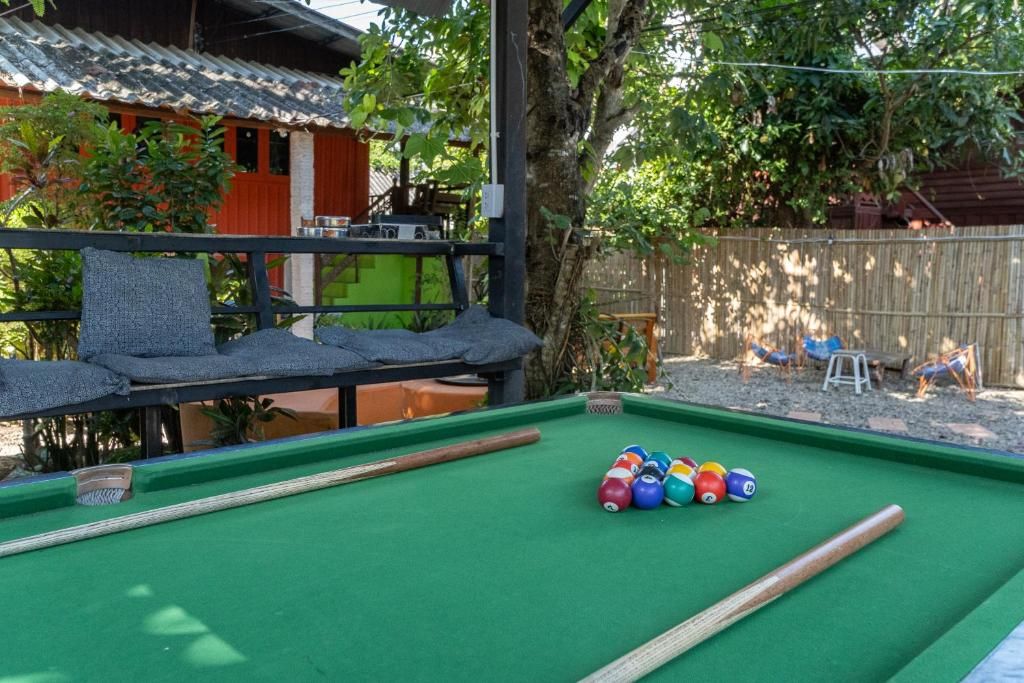 A pool table with billiard balls and cues, surrounded by a wooden fence and a building with a red roof.
