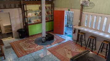 A room with a central column, a bookshelf, a small table with a kettle, and a window with a view.