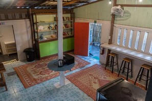 Habitación con una columna central, una estantería, una mesita con hervidor y una ventana con vistas.