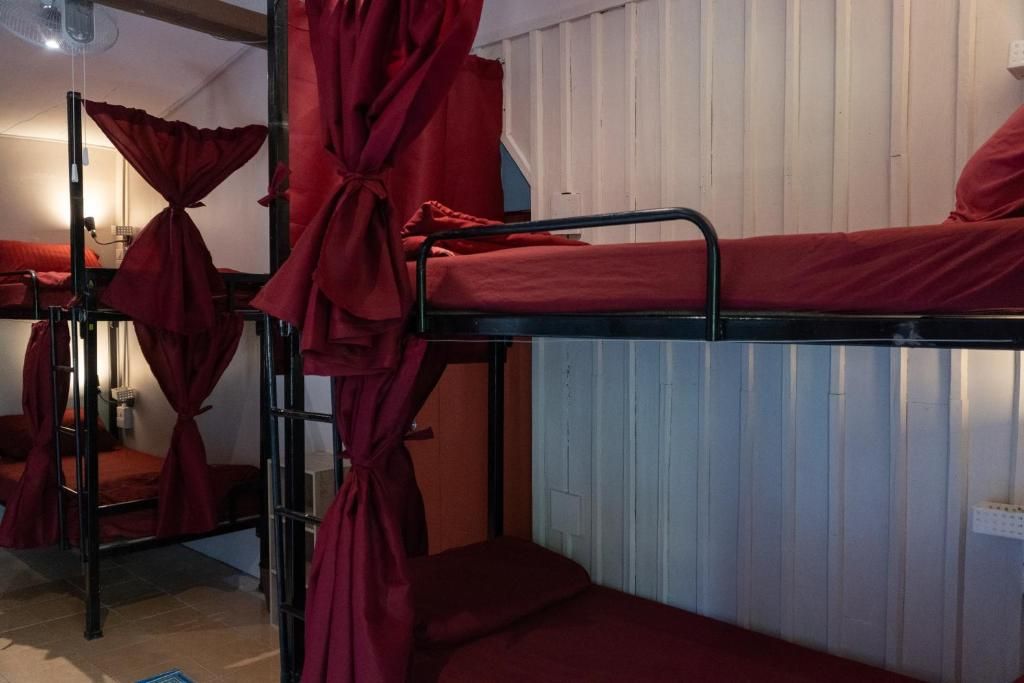 A bunk bed room with red bedding and curtains, a ceiling fan, and a white wall with a calendar.