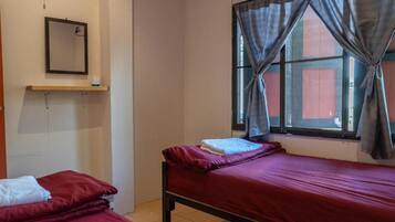 Una habitación sencilla con dos camas, una ventana con cortinas, un estante en la pared con un espejo y un mueble pequeño con artículos de aseo.