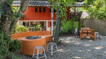 Un bâtiment de style japonais traditionnel, avec une façade rouge, un banc en bois et un petit espace extérieur aménagé avec des tabourets.