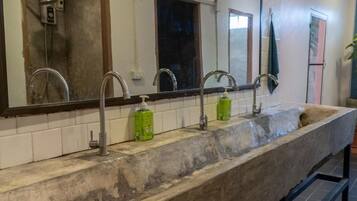 Une salle de bain avec un grand miroir, trois lavabos et une douche.