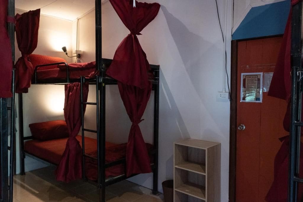 Une chambre de dortoir avec des lits superposés, une petite étagère et une porte ornée d’une affiche.