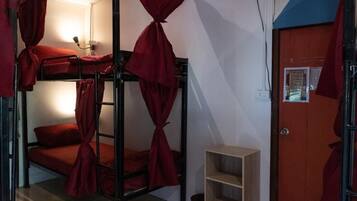 Une chambre de dortoir avec des lits superposés, une petite étagère et une porte ornée d’une affiche.