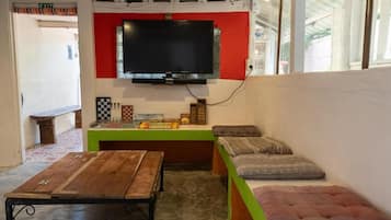 A room with a television mounted on a red wall, a wooden table, a bench with cushions, and a green bench.