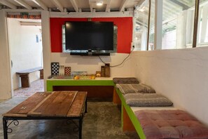 Una habitación con una televisión montada en una pared roja, una mesa de madera, un banco con cojines y un banco verde.