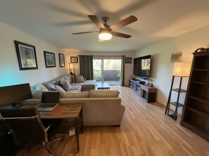 A modern living room with a sofa, a coffee table, a TV, and a ceiling fan. - Ocean Breeze, quiet, roomy condo, 1 mile walk to Ocean Beach! (San Diego)