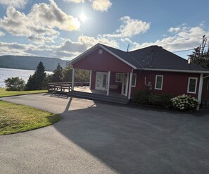 A red building with a covered porch, a bench, and a view of a lake. - Mae’s place l Horse Chops Pond Retreat (Cape Broyle)
