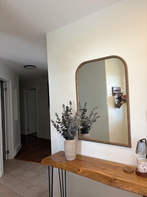 A hallway with a wooden console table, a mirror, and a potted plant. - Mae’s place l Horse Chops Pond Retreat (Cape Broyle)