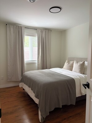 A bedroom with a bed, curtains, a window with blinds, and a door.