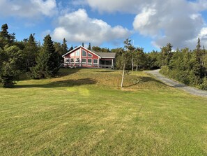 Ein rotes Haus mit einer Veranda, umgeben von einer Rasenfläche und Bäumen.