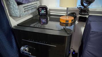 A compact, modern room with a bed, a small table with a lamp, a charging station, and a digital clock.