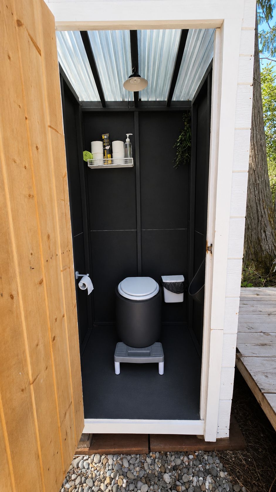 A compact outdoor bathroom with a black toilet, a small step stool, and a shelf with toiletries.