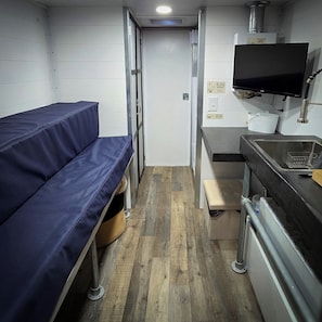 A compact kitchenette with a sink, stove, and a flat-screen TV mounted above it.