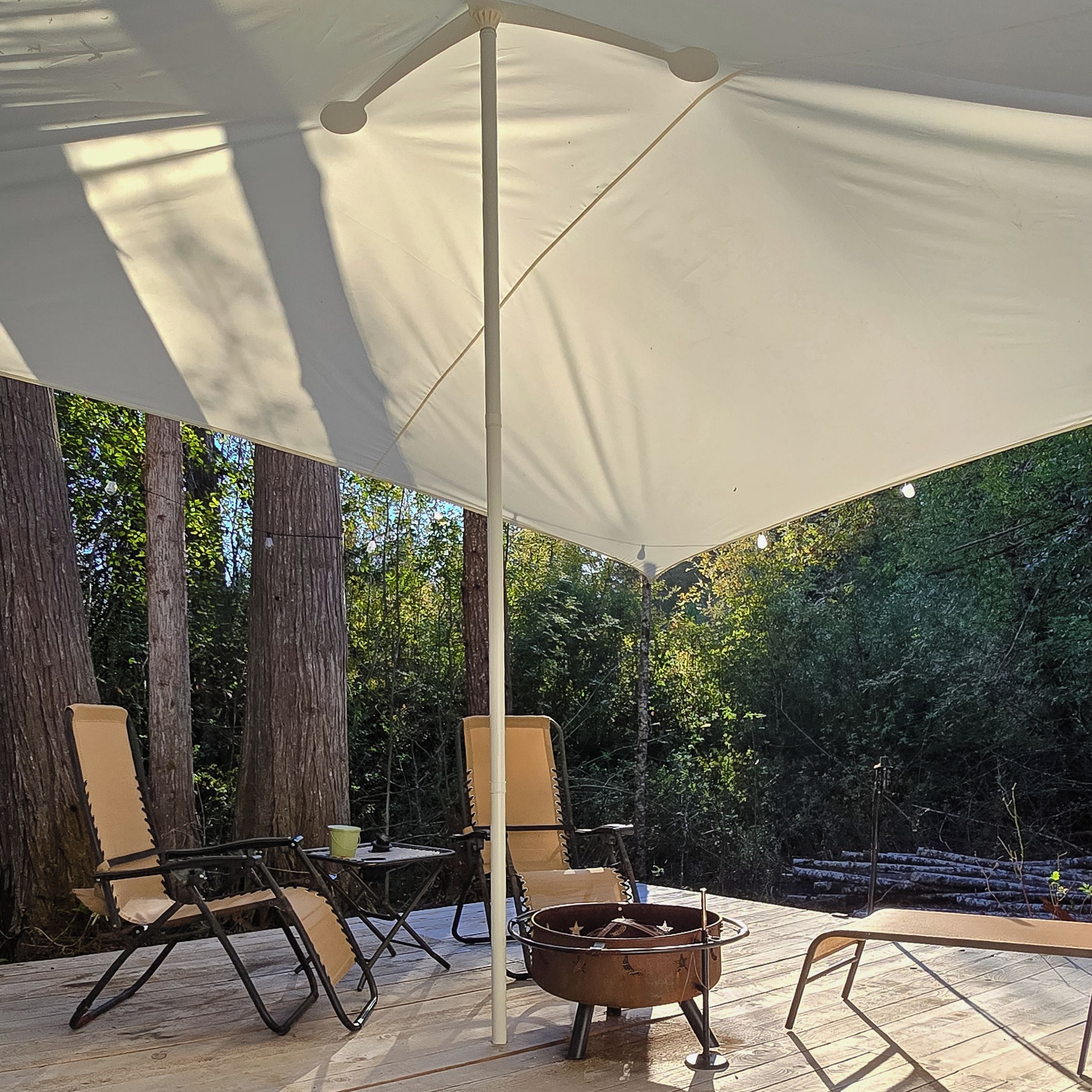 An outdoor seating area with a white canopy, two folding chairs, a small table, and a fire pit.