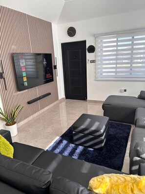 Una sala moderna con un televisor de pantalla plana montado en una pared, una puerta negra y un ventanal con persianas.