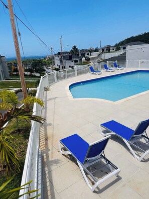 A swimming pool with blue lounge chairs and a white fence. - Cozy 2-bedroom bungalow with AC in charming Runaway Bay. Hosts up to 4  persons. (Runaway Bay)