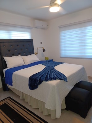 A bedroom with a bed, bedside lamp, air conditioning unit, and a window with blinds. - Cozy 2-bedroom bungalow with AC in charming Runaway Bay. Hosts up to 4  persons. (Runaway Bay)