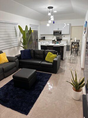 A modern living room with a sofa, ottoman, and a dark rug. - Cozy 2-bedroom bungalow with AC in charming Runaway Bay. Hosts up to 4  persons. (Runaway Bay)