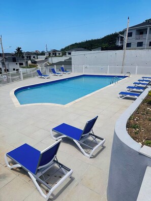 Piscina con agua azul, rodeada de barandillas blancas y sillas reclinables azules.